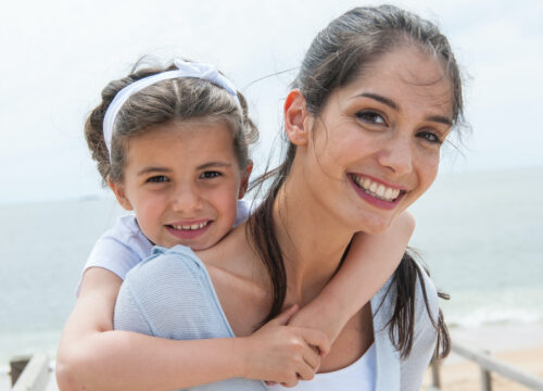 Photo of a mother and daughter smiling by the beach