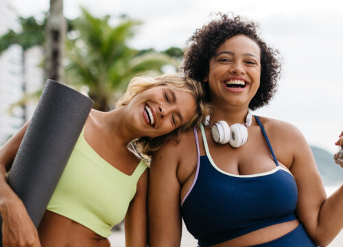 Photo of two happy women in workout clothes outside by the beach